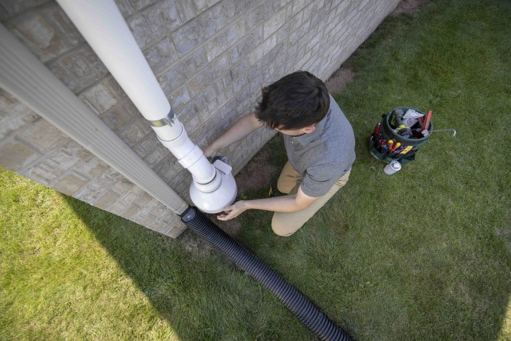 Technician installing a radon mitigation system on the exterior of a residential home with tools nearby